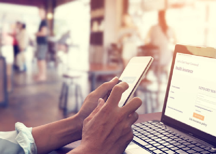 hand-holding-phone-in-front-of-computer-blurry-background