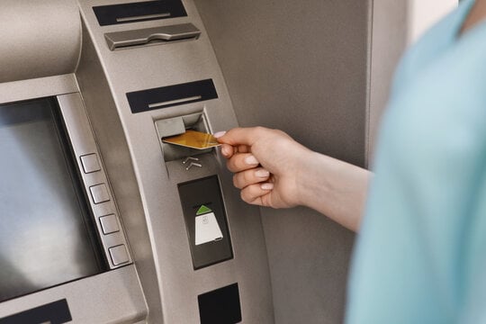 Close up of a person inserting her debit card to access her personal checking account at the ATM