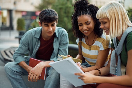 Three college students reviewing financial documents together outside on campus