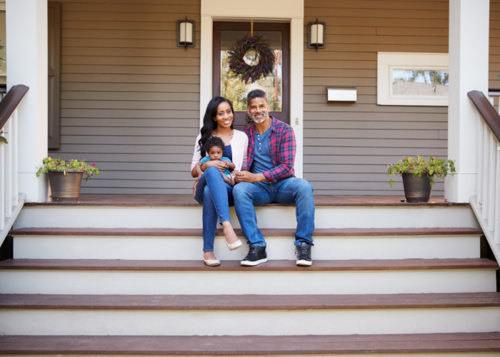 New family sitting on the steps of the front porch of their new home