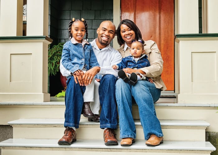 Close up shot of a couple with their two daughters sitting on the front porch of their home
