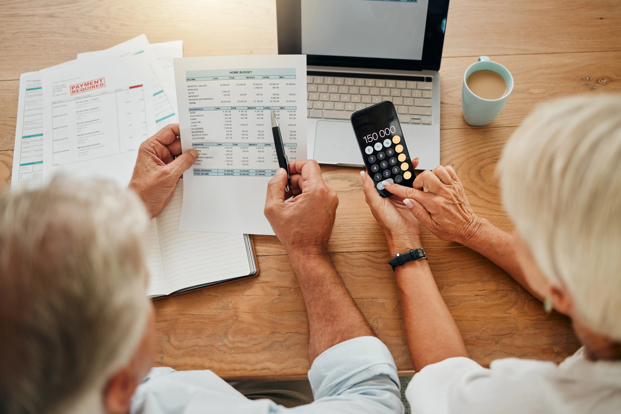 Two seniors reviewing their household budget and expenses with a calculator, laptop, and smartphone