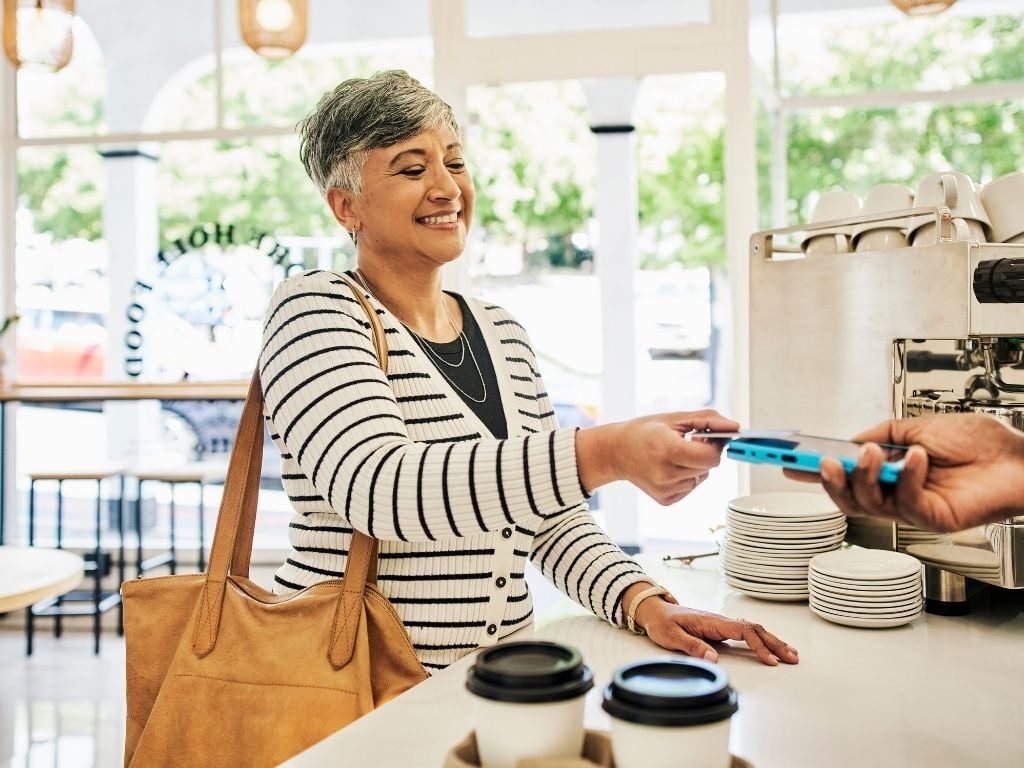 Woman making a contactless payment by tapping her card at a checkout terminal