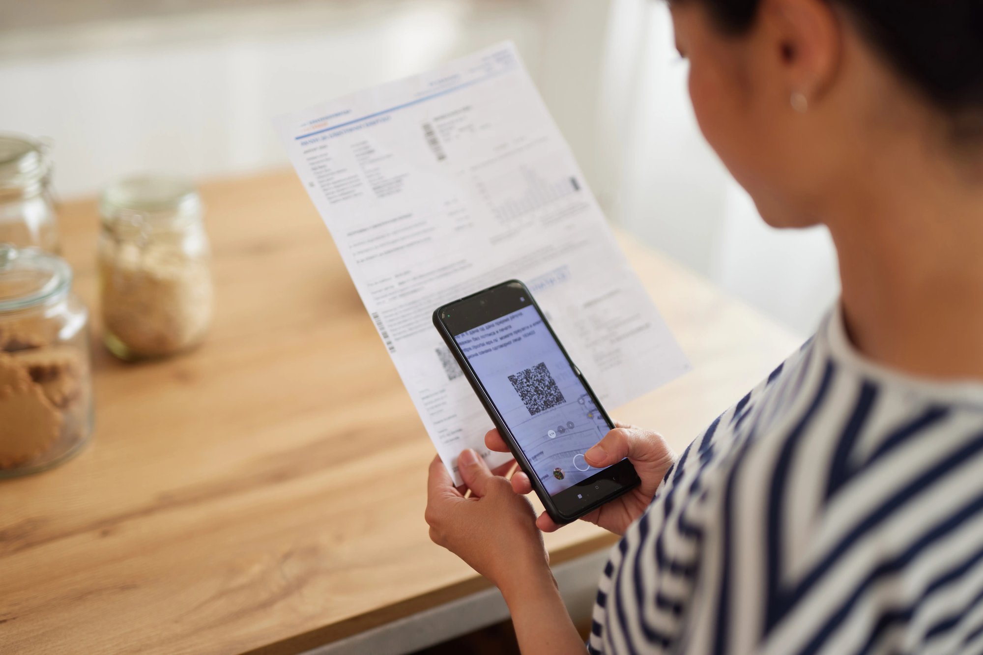 A woman scanning a QR code using her smartphone in order to pay a utility bill