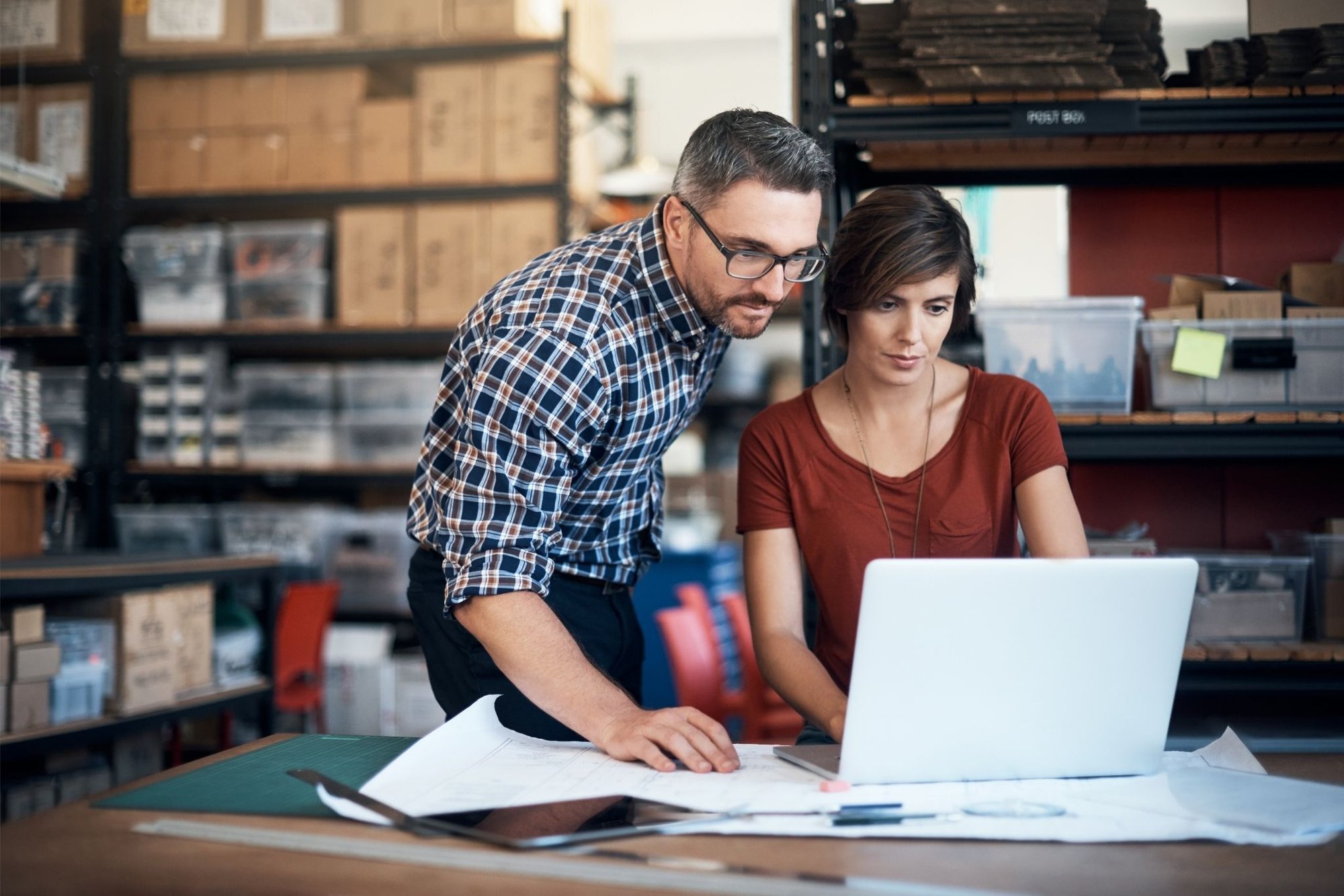 Two business owners collaborating and reviewing documents on a laptop in their workspace