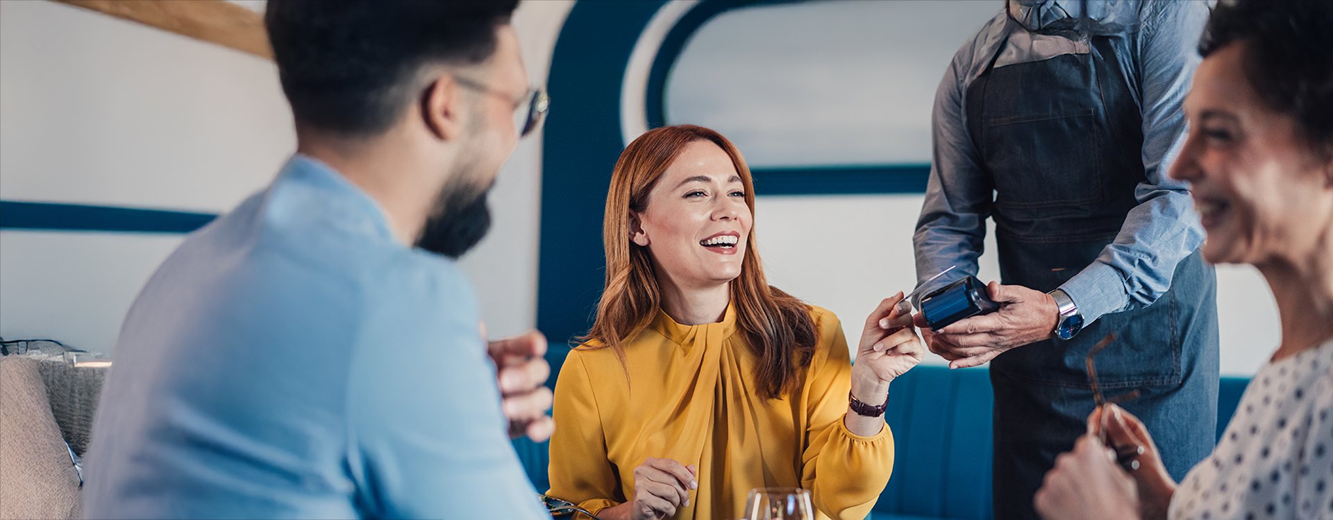 A woman using her credit card for tap-to-pay while sitting and laughing with another man and woman