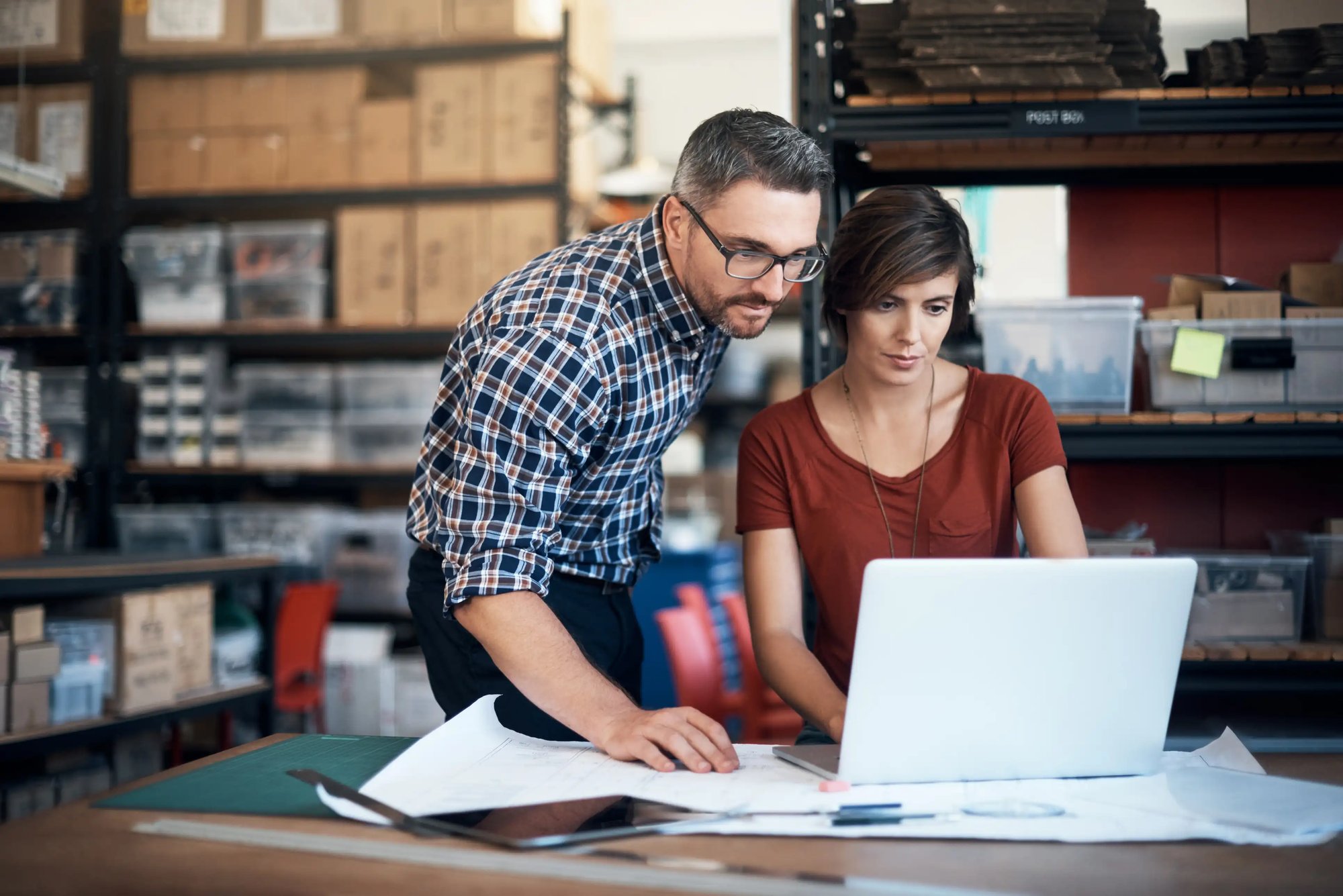 Two business professionals reviewing inventory information on a laptop in a stock room