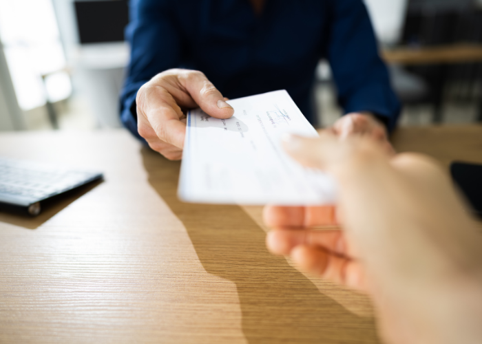 Person handing a check to another person, closeup of hands.