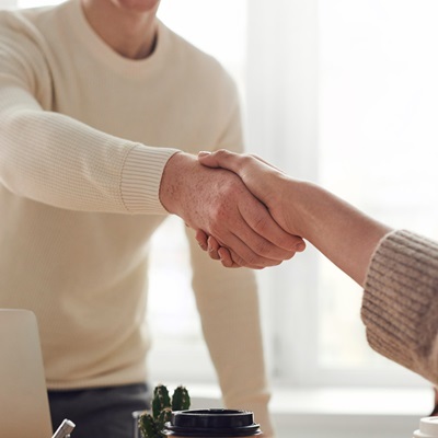 Two people shaking hands in a professional setting, symbolizing agreement, partnership, or collaboration.