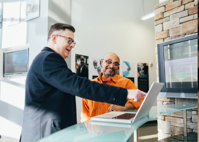 Person pointing to a laptop on a desk.