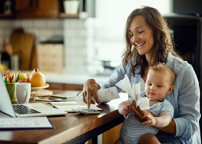 Person reviewing household finances while holding a baby, planning for retirement income.